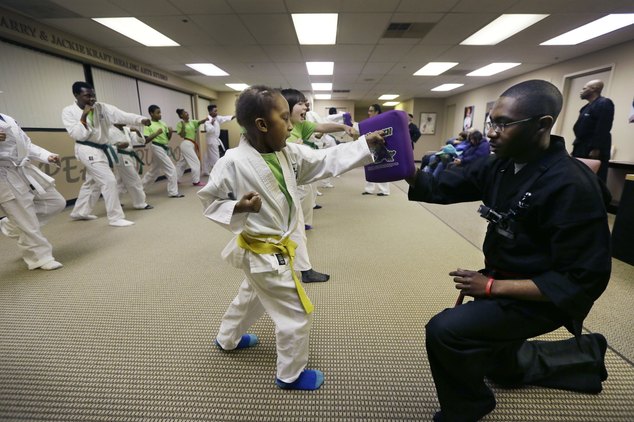 Child in martial arts uniform punching pad held by instructor.