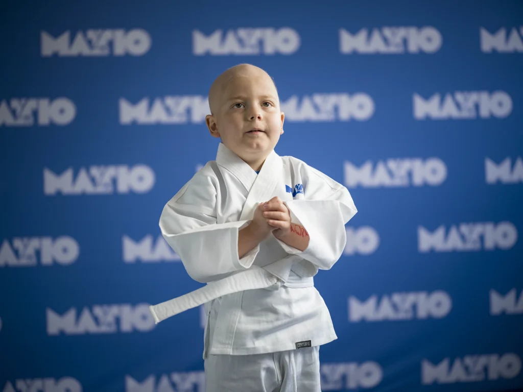 Young child in martial arts uniform standing with hands clasped.
